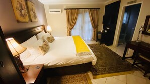 Habitación de hotel con una cama grande, una mesita de noche con lámpara, un tapete pequeño y vistas al baño.