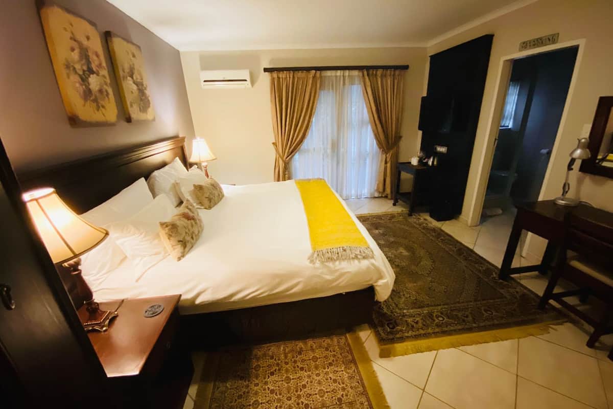 Habitación de hotel con una cama grande, una mesita de noche con lámpara, un tapete pequeño y vistas al baño.