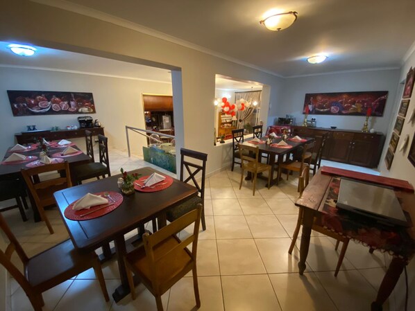 Un comedor con varias mesas y sillas, una zona de cocina con armarios y una escalera que sube a un nivel superior.