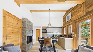 A modern interior with a stone fireplace, wooden beams, a dining area, and a kitchen. - Les Gets - Lovely apartment with balcony and fireplace near the slopes (Les Gets)