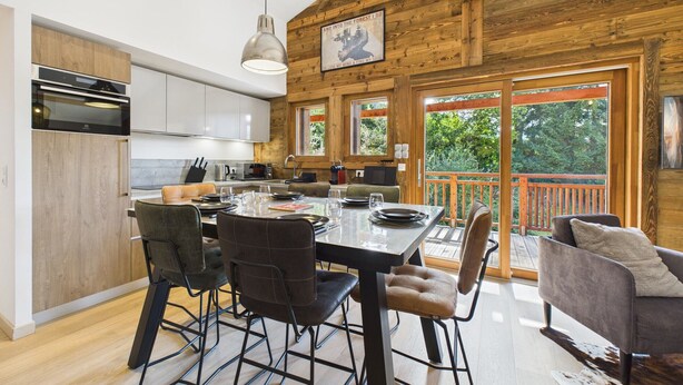 A modern kitchen with wooden beams, a dining area with a table set for four, and a large window overlooking a deck. - Les Gets - Lovely apartment with balcony and fireplace near the slopes (Les Gets)