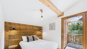 A bedroom with a wooden headboard, a bed with white bedding, a bedside table, a lamp, and a view of a balcony with a wooden railing. - Les Gets - Lovely apartment with balcony and fireplace near the slopes (Les Gets)