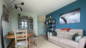 A living room with a dining table, chairs, a sofa, a bookshelf, and a floor lamp. - 1-bedroom apartment with WIFI, parking, pets allowed in Perros-Guirec (Perros-Guirec)