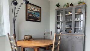 A dining area with a round wooden table, four chairs, a painting on the wall, and a grey cabinet with glass doors. - 1-bedroom apartment with WIFI, parking, pets allowed in Perros-Guirec (Perros-Guirec)