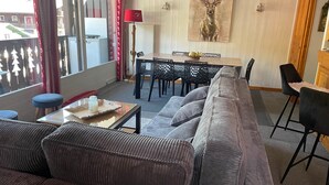 Un salon comprenant un canapé, une table à manger avec des chaises, une lampe et un tableau représentant un cerf accroché au mur.