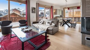 A modern living room with a glass coffee table, a sofa with decorative pillows, and a view of snowy mountains through large windows. - Luxury Apartment, 3 Bedrooms, Close to Slopes, Sauna (Méribel)