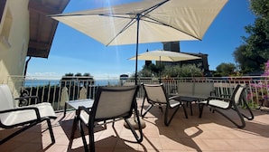 Un patio al aire libre con una mesa, sillas y un paraguas grande, con vista al mar.
