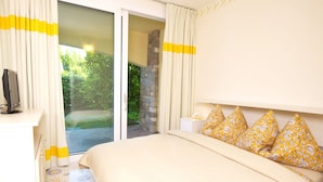 Un dormitorio con cama, televisor sobre un mueble, pared de piedra y vistas a la vegetación por un ventanal.