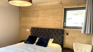Une chambre à coucher avec une tête de lit en bois, un lit avec une literie blanche, une chaise et une fenêtre avec des rideaux.