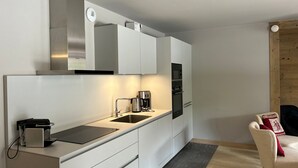 Une cuisine moderne avec des armoires blanches, une hotte de cuisinière en acier inoxydable, une machine à café et un four encastré.