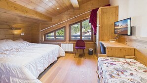 A wooden cabin room with two beds, a desk, a chair, a TV, and large windows.