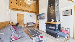 A cozy living room with a fireplace, wooden ceiling, and a sofa with cushions.