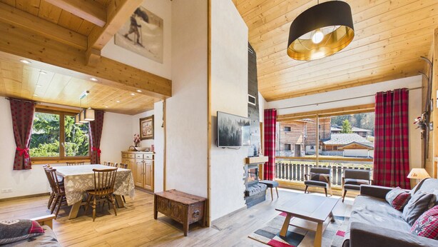 A spacious living area with a wooden ceiling, a dining table, a sofa, and a view of the outdoors.