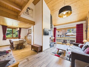 Amplia sala de estar con techo de madera, una mesa de comedor, un sofá y vistas al exterior.