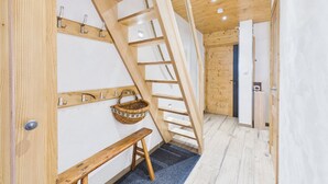 A wooden interior with a sloped ceiling, a bench, a basket, and a door.