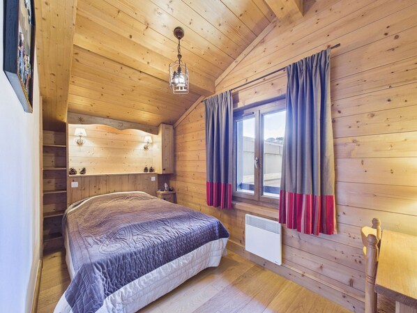 Un dormitorio de cabaña de madera con cama, una ventana con cortinas, un calentador fijado a la pared y una lámpara colgante.