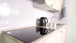 Una cocina con un hervidor eléctrico negro, una cafetera y dos tazas blancas sobre una encimera reflectante.