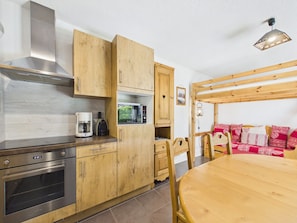 A kitchen with wooden cabinets, a microwave, a coffee maker, and a dining area with a wooden table and chairs. - Central Les Gets Apartment with Terrace, Garage and WIFI (Les Gets)