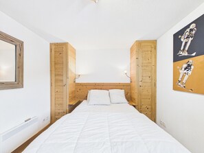 Ein Schlafzimmer mit hölzernem Kopfteil, einem Bett mit weißer Bettwäsche, einer Wandleuchte und einem gerahmten Bild an der Wand.