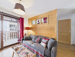 Une pièce chaleureuse avec un mur en bois, un canapé, une table sur laquelle sont posés divers objets et une porte.