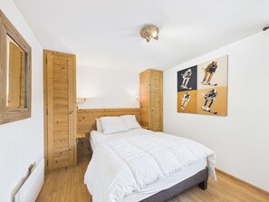 A bedroom with a wooden headboard, a bed with white bedding, a wall-mounted light fixture, and a ski-themed artwork. - Central Apartment in Les Gets - Near Ski Lifts, Shops, and Amenities (Les Gets)