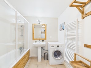 A bathroom with a glass-enclosed shower, a sink with a mirror, a washing machine, and a drying rack.