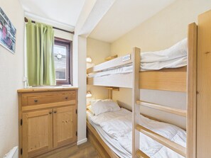 Une petite pièce avec un lit superposé, une commode en bois et une fenêtre avec des rideaux.