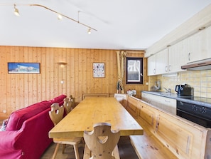 A wooden interior with a dining table, red sofa, and kitchen area including a stove and cabinets.