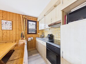 A kitchen with wooden cabinets, a built-in oven, a coffee maker, and a window with a view of a building. - Ski-in/Ski-out Apartment in Les Gets, 50m from Village Center, Sleeps 6, Balcony, Garage, WiFi (Les Gets)
