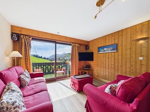 A living room with a red sofa set, a flat-screen TV, and a wooden paneled wall. - Ski-in/Ski-out Apartment in Les Gets, 50m from Village Center, Sleeps 6, Balcony, Garage, WiFi (Les Gets)