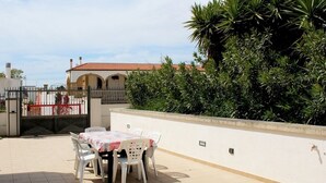 Eine Terrasse im Freien mit Tisch und Stühlen, einer weißen Wand und einem Tor.