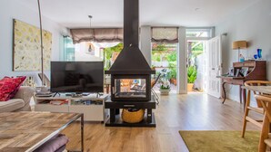 Ein Wohnzimmer mit Holzofen in Schwarz, einem Fernseher und einem Sofa. Es gibt einen Essbereich mit Tisch und Stühlen.