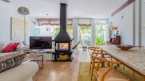 Ein Wohnzimmer mit einem schwarzen Kaminofen, einem Fernseher, einer Couch und einem Essbereich mit Tisch und Stühlen.