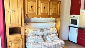 A compact kitchen with wooden cabinets, a built-in bench with patterned cushions, a small refrigerator, and a microwave.