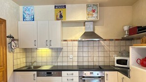 A kitchen with white cabinets, a Bosch dishwasher, an oven, and a microwave. There are posters on the wall and a red kettle on the counter. - Ski-in/Ski-out Apartment with Terrace & Summer BBQ, Near Village Center (Les Gets)
