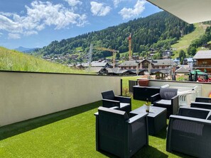 A terrace with outdoor furniture and a view of a village and mountains. - Ski-in/Ski-out Apartment with Terrace & Summer BBQ, Near Village Center (Les Gets)
