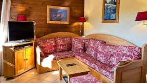 A cozy room with a wooden sofa, a TV, and a cabinet. - Ski-in/Ski-out Apartment with Terrace & Summer BBQ, Near Village Center (Les Gets)