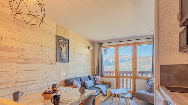 Una habitación acogedora con pared de madera, un sofá, una mesa de comedor con sillas y vistas a montañas a través de grandes ventanales.