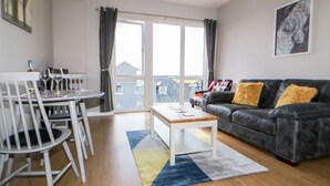 Un salon moderne comprenant un coin repas, un canapé en cuir noir et une grande fenêtre avec des rideaux.
