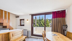 A wooden dining table with chairs, a bench, a small window, and a sliding glass door with a view of trees. - Spacious apartment in the center, 6 guests (Les Gets)