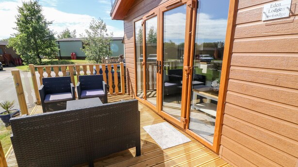 A wooden deck with wicker furniture and a glass door leading to a patio area. - Eden Lodge - Sherwood 21 (Carnforth)