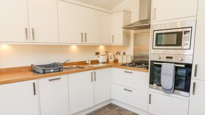 A modern kitchen with white cabinets, a wooden countertop, a gas stove, a microwave, and a kettle. - Eden Lodge - Sherwood 21 (Carnforth)