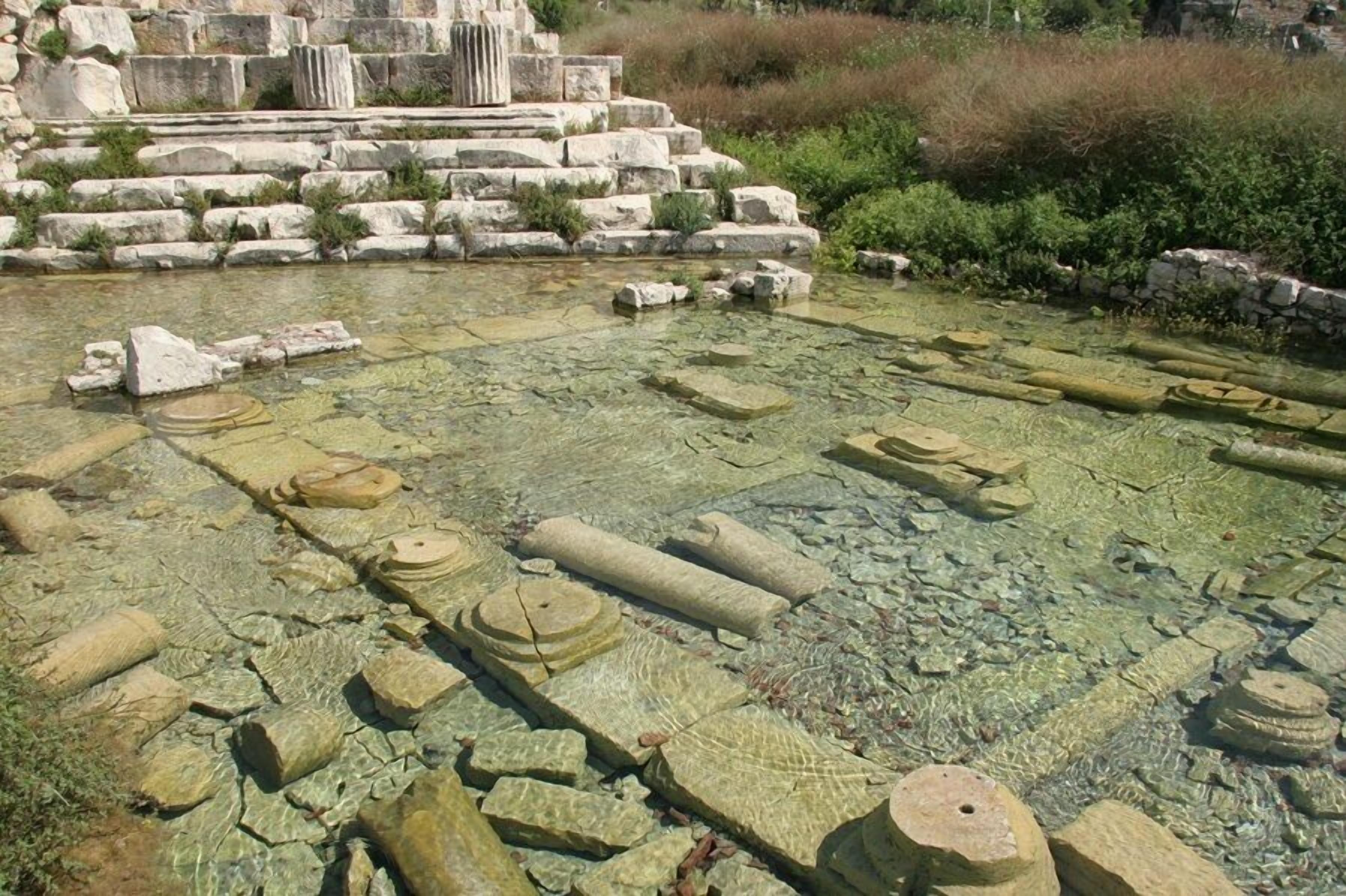 Ancient ruins with stone structures and a partially visible water feature.