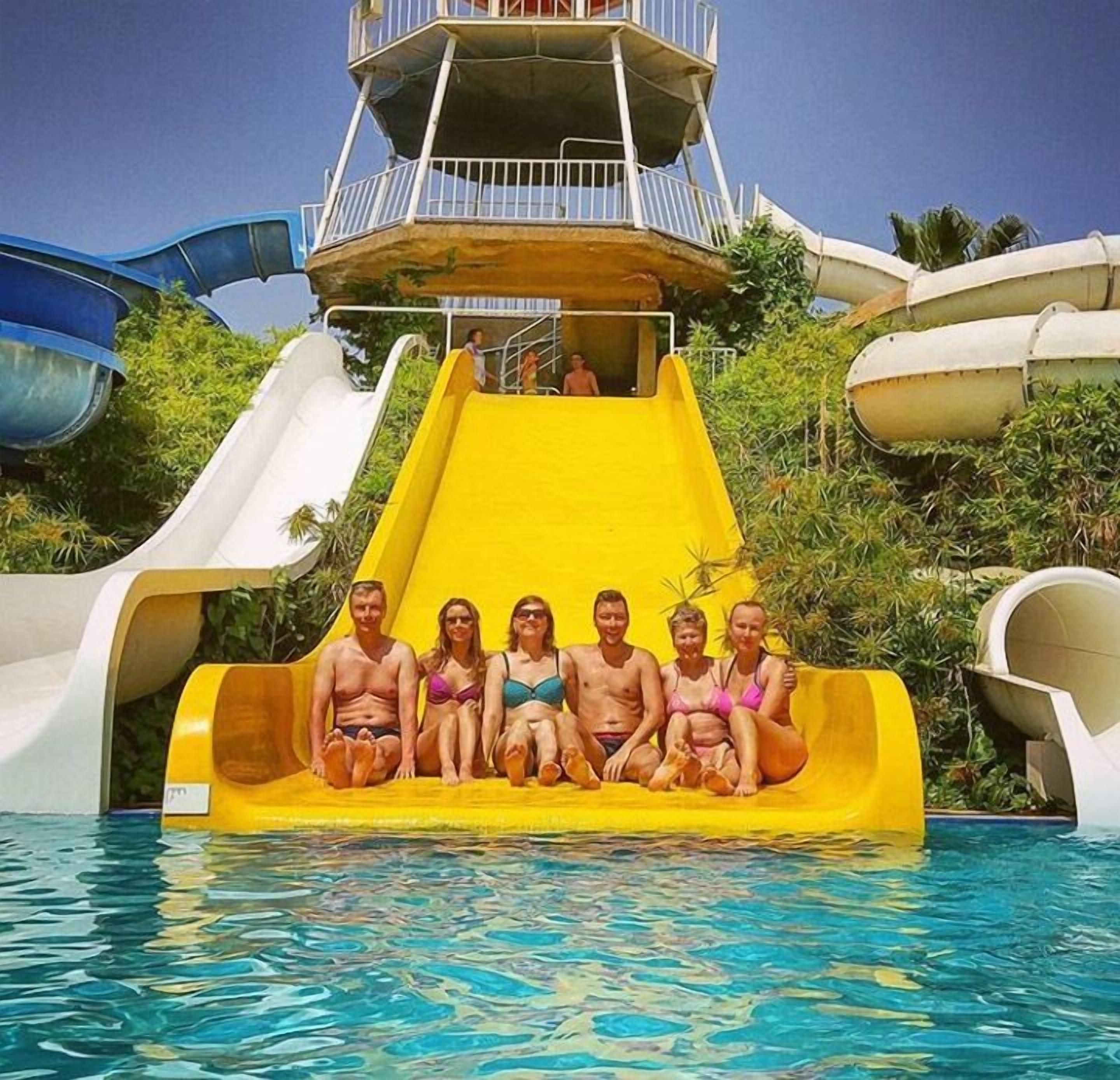 A group of people sitting on a yellow water slide at a water park.