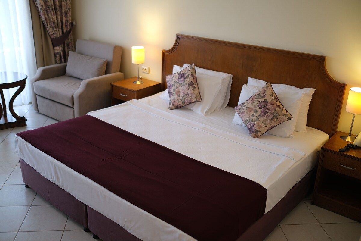 A hotel room with a large bed, two nightstands, a chair, and a lamp.