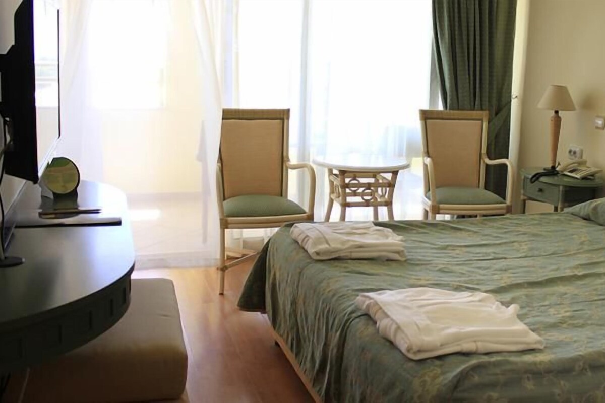A hotel room with a bed, two chairs, a small table, a lamp, and a desk with a computer.