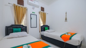 A hotel room with two beds, each with a headboard, a window with curtains, a wall-mounted air conditioner, and a small Eiffel Tower decoration. - Homestay Jogja Dekat Masjid Jogokaryan by Simply Homy (Yogyakarta)