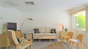 Un salon moderne comprenant un canapé, deux fauteuils, une table basse, un téléviseur et une lampe.