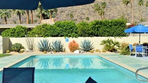 Une piscine entourée de chaises longues et de parasols, le tout agrémenté d’un aménagement paysager luxuriant et de palmiers.