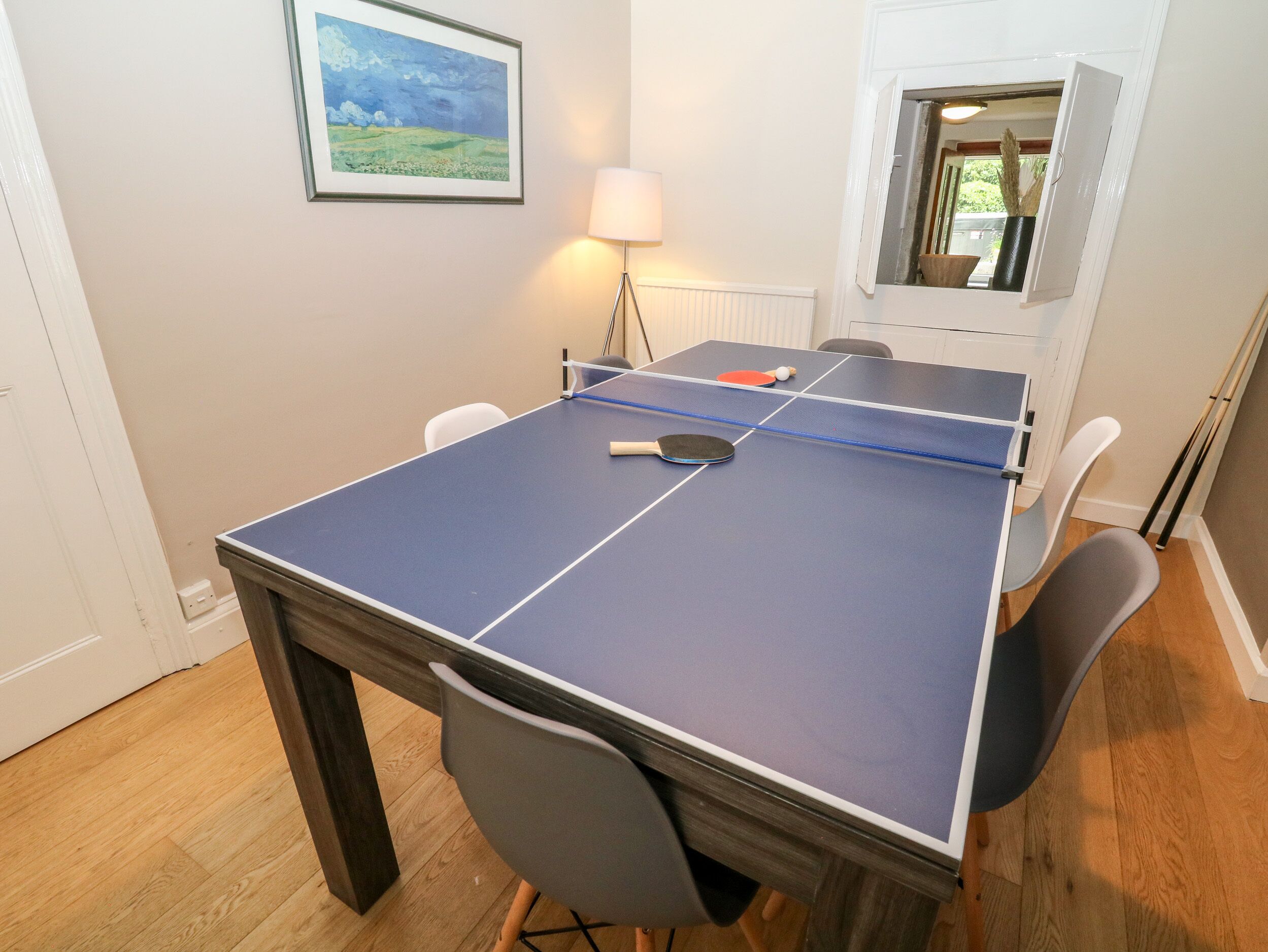 A ping pong table with two paddles and a ball, surrounded by four chairs.
